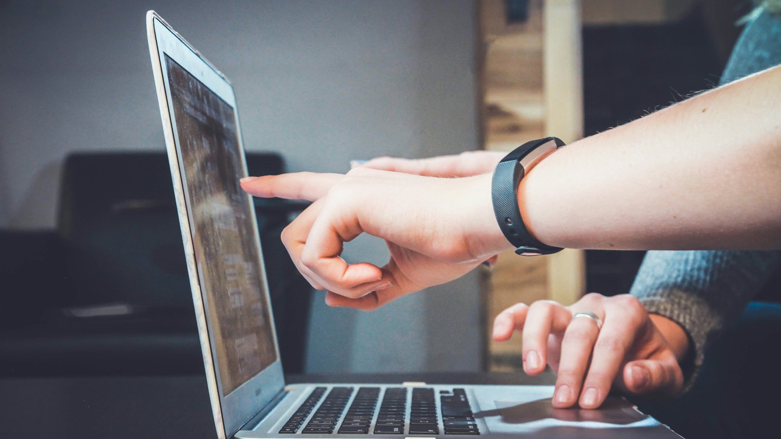 A hand pointing at a laptop screen next to a wristwatch